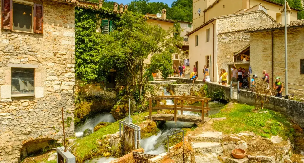 Un borgo incantevole in Umbria, tra i più belli d'Italia, con un ruscello che attraversa le case in pietra e un ponticello di legno.