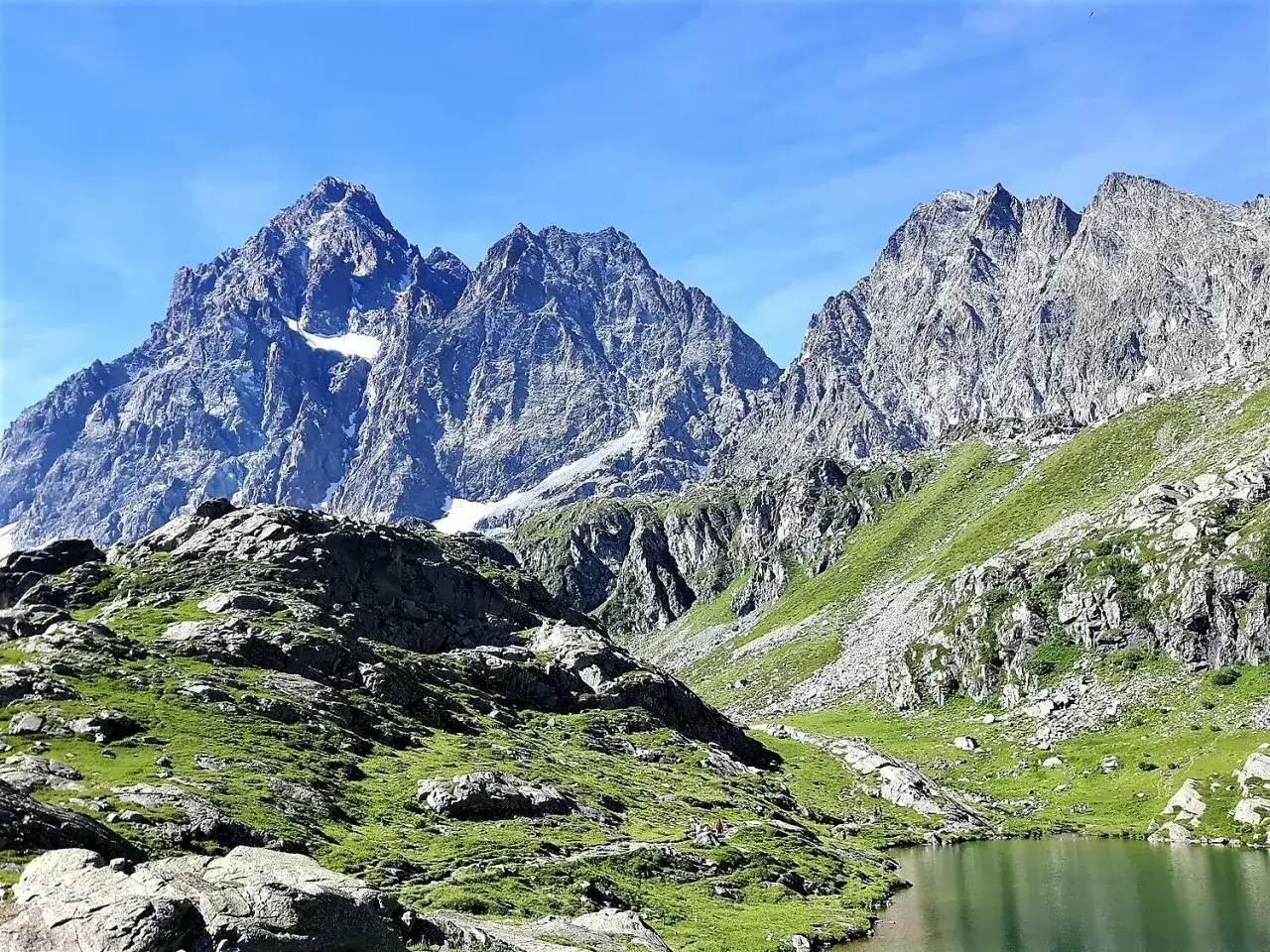Un lago alpino riflette montagne imponenti e prati verdi. Un luogo ideale tra i posti da visitare in Piemonte per immergersi nella natura incontaminata.