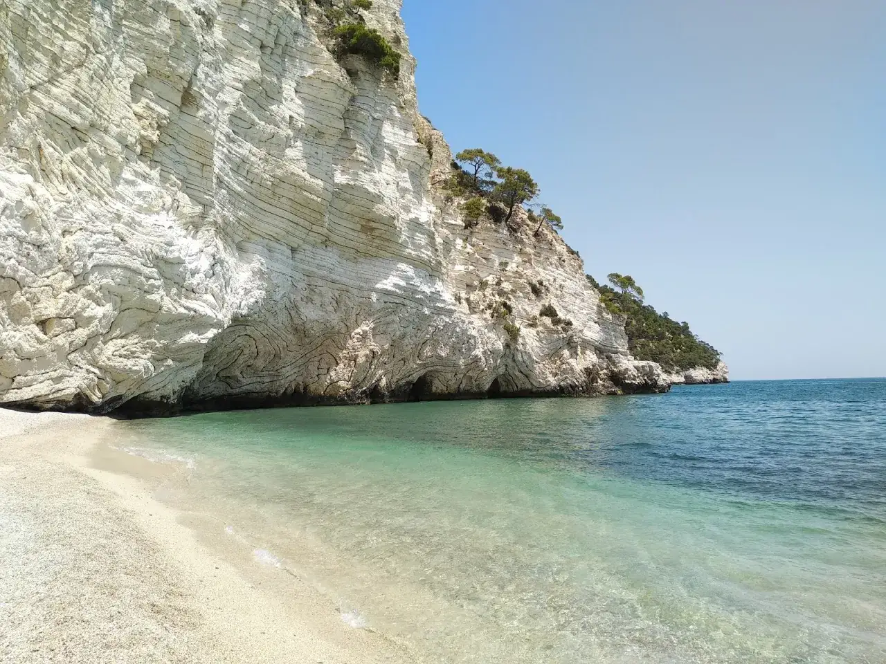 Spiaggia di ciottoli bianchi e mare cristallino ai piedi di una maestosa scogliera calcarea, con grotte marine. La cala della pipa, un angolo di paradiso.
