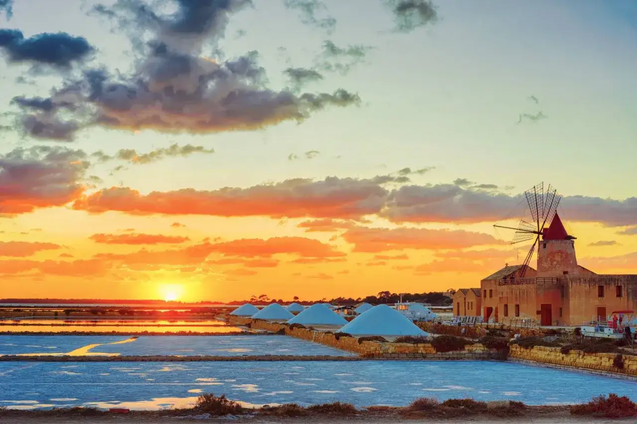 Saline di Trapani al tramonto: mulino a vento, cumuli di sale e specchi d'acqua. Un'idea di cosa vedere a Trapani in un giorno.