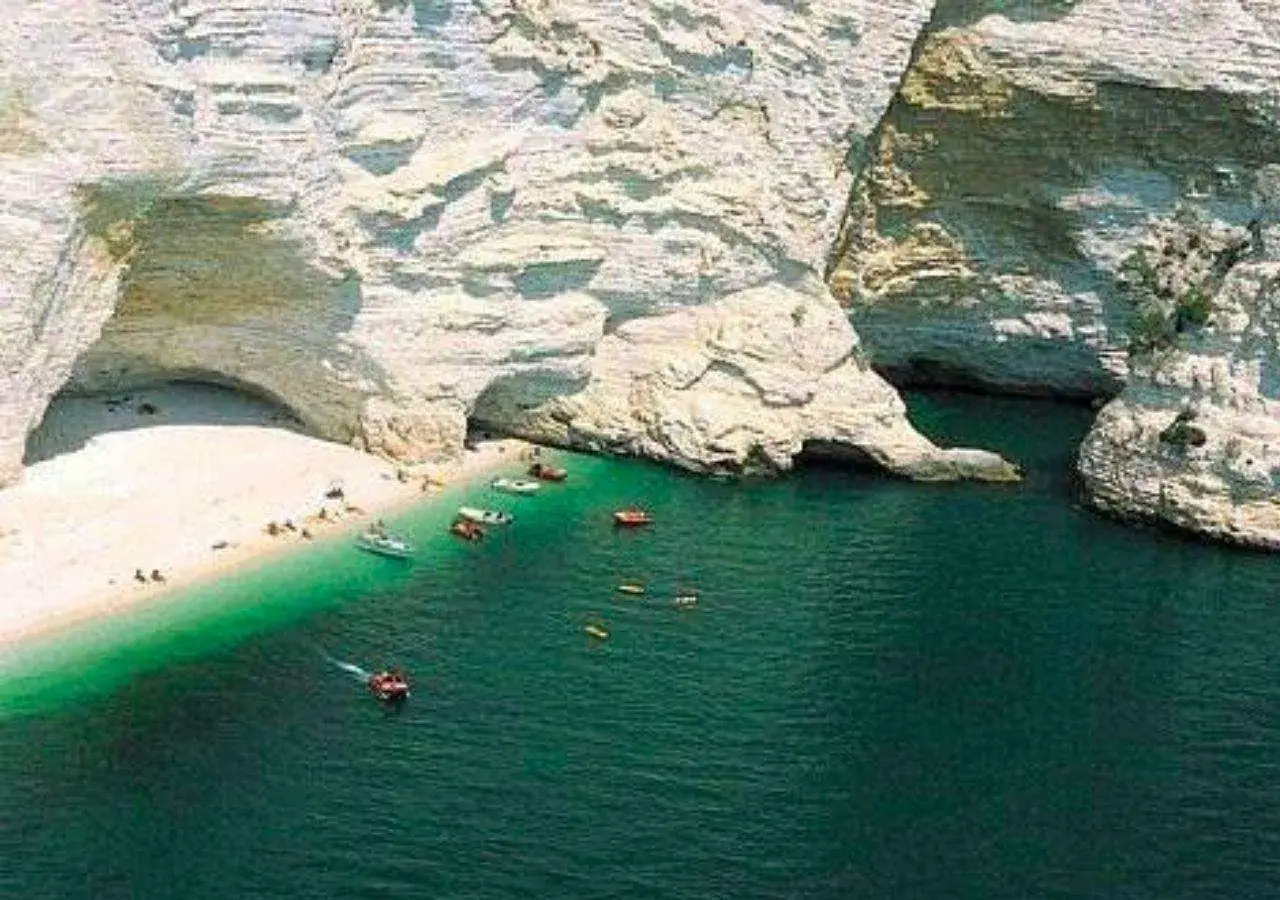 Spiaggia bianca incastonata tra alte rocce calcaree, acque verdi e trasparenti, barchette e persone che godono del sole. Un angolo di paradiso da scoprire tra le cose da vedere a Manfredonia.