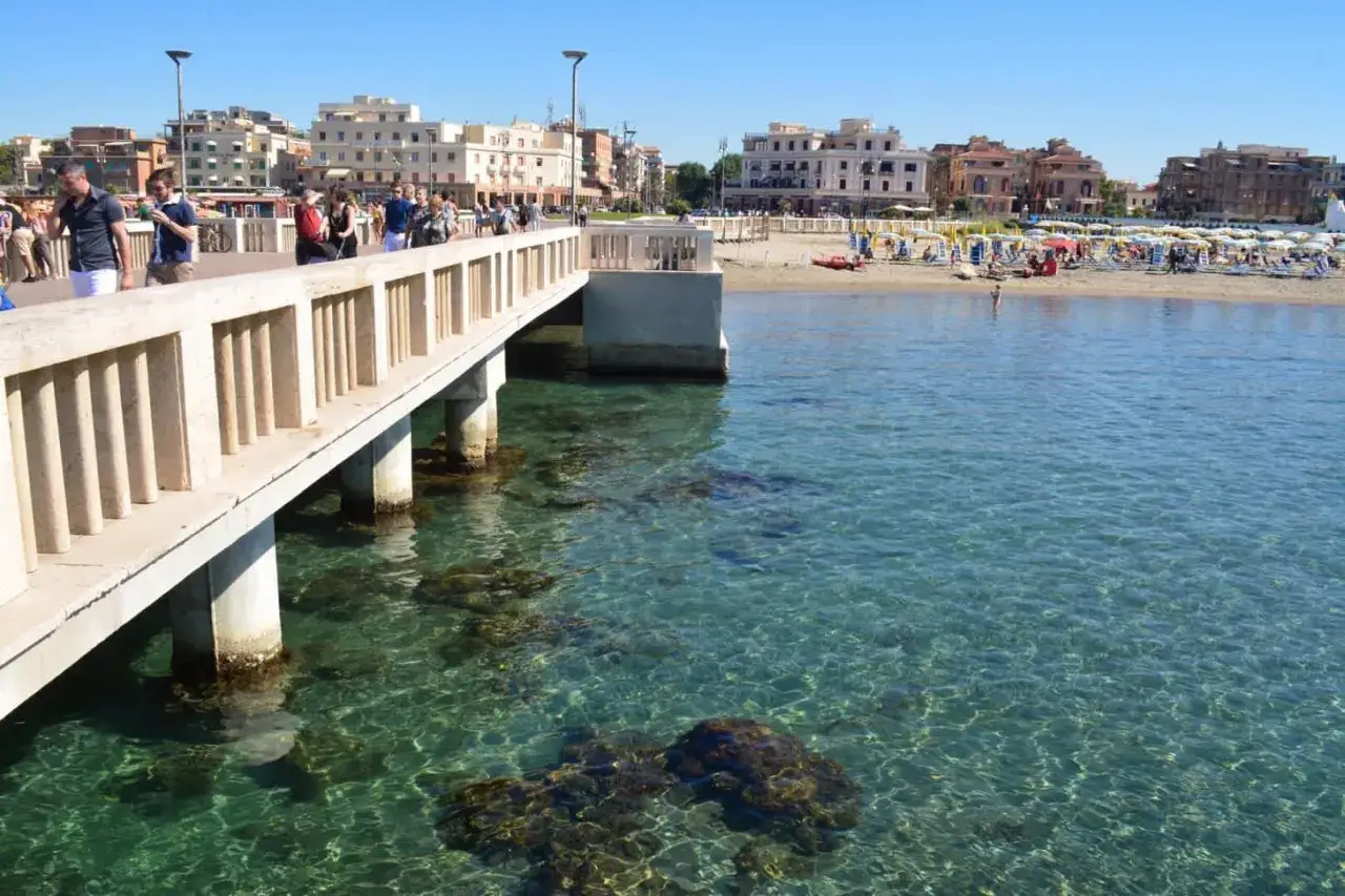 Passeggiata sul molo con vista sulla spiaggia e sul mare cristallino. A Roma c'&egrave; il mare, un'oasi di pace.