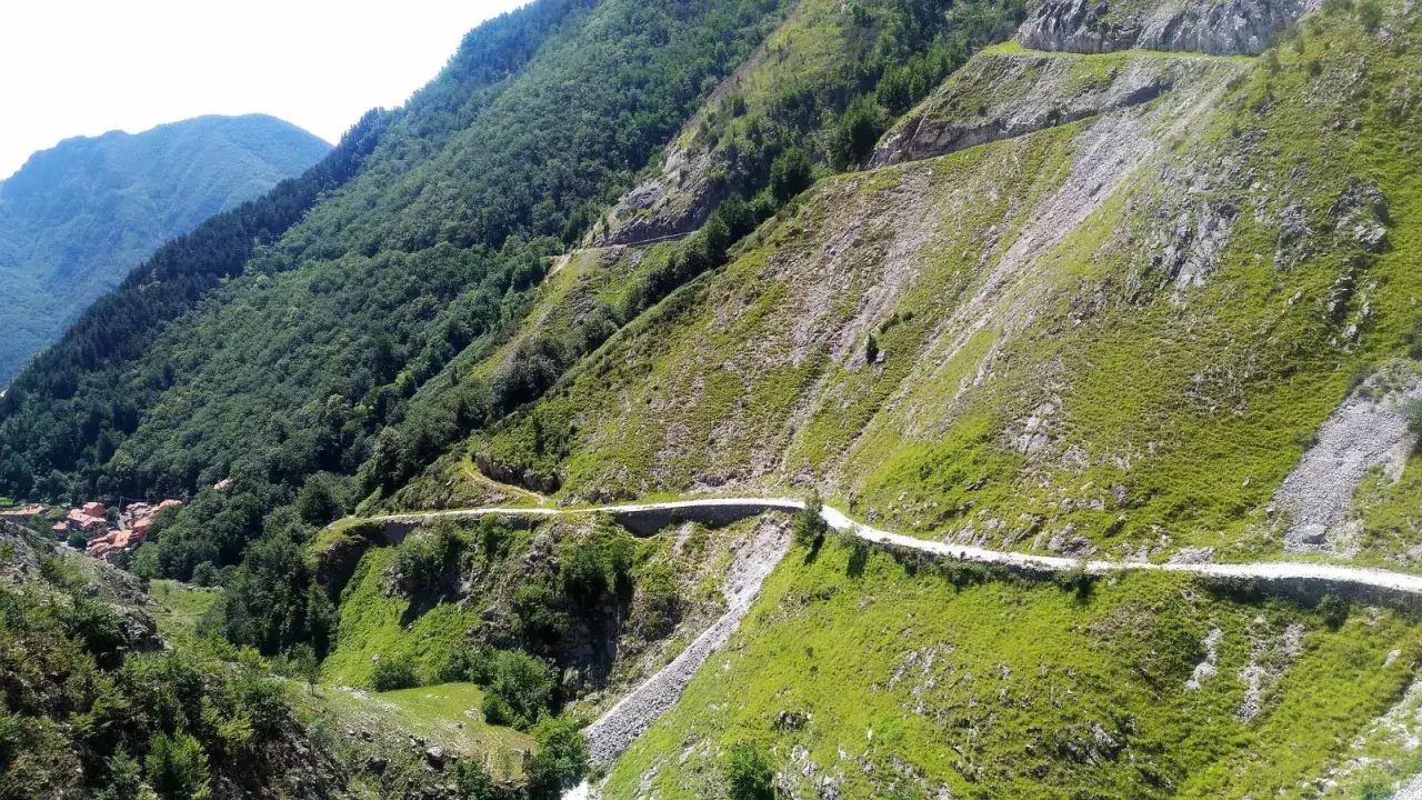 Strada tortuosa che si snoda tra montagne verdi, con un villaggio in lontananza. Le tappe della via Vandelli offrono panorami mozzafiato.