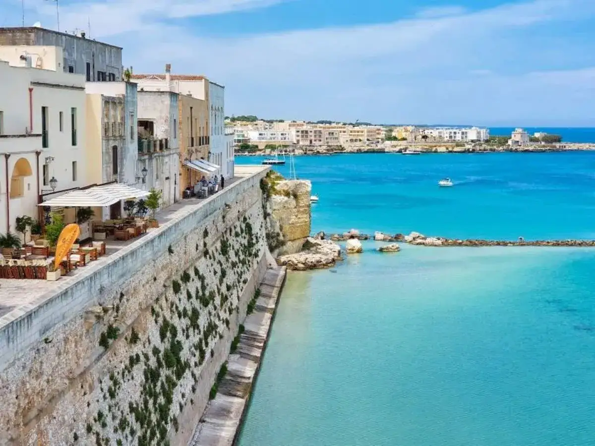 Otranto cosa vedere: un lungomare con ristoranti affacciati sul mare cristallino e il borgo antico sullo sfondo.