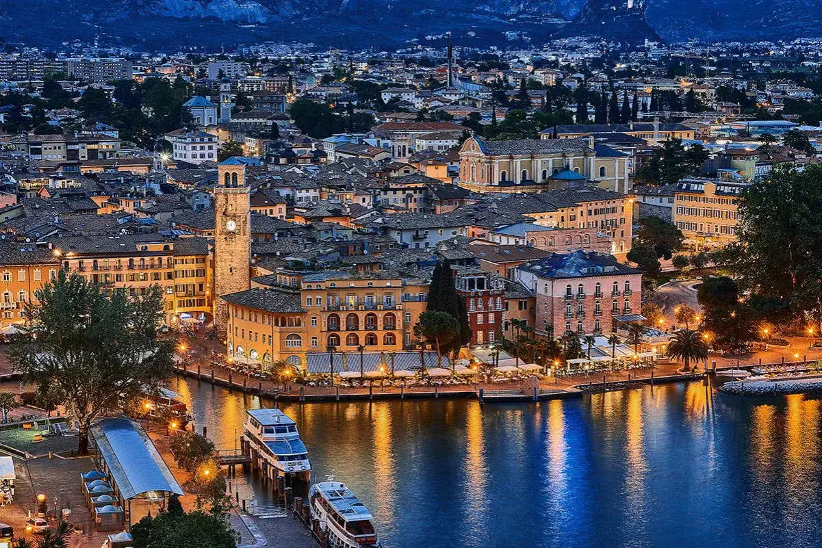 Incantevole panorama serale di un paese sul lago, con edifici colorati, un campanile e riflessi sull'acqua. Un gioiello tra i paesi trentino alto adige.
