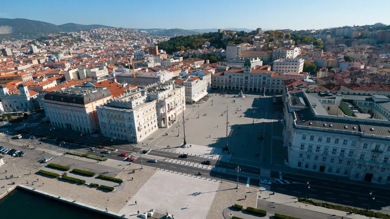 Ampia vista aerea della Piazza Unità d'Italia a Trieste, con i suoi palazzi storici affacciati sul mare e la città che si estende sulle colline.