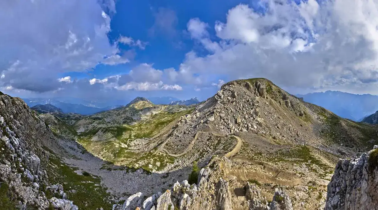 Sentiero tortuoso tra rocce e prati verdi, ideale per passeggiate in Veneto. Panorami mozzafiato sotto un cielo azzurro con nuvole bianche.
