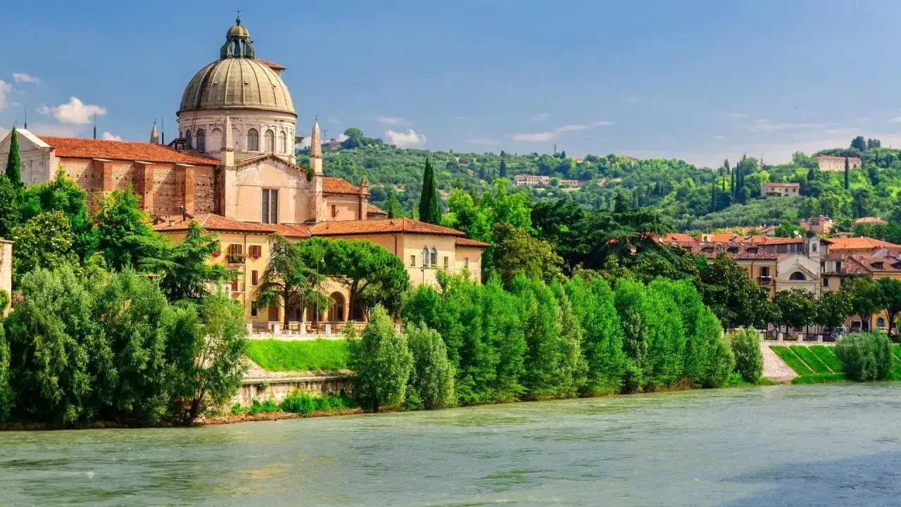 Un borgo del Veneto con una chiesa a cupola, alberi verdi e il fiume Adige.