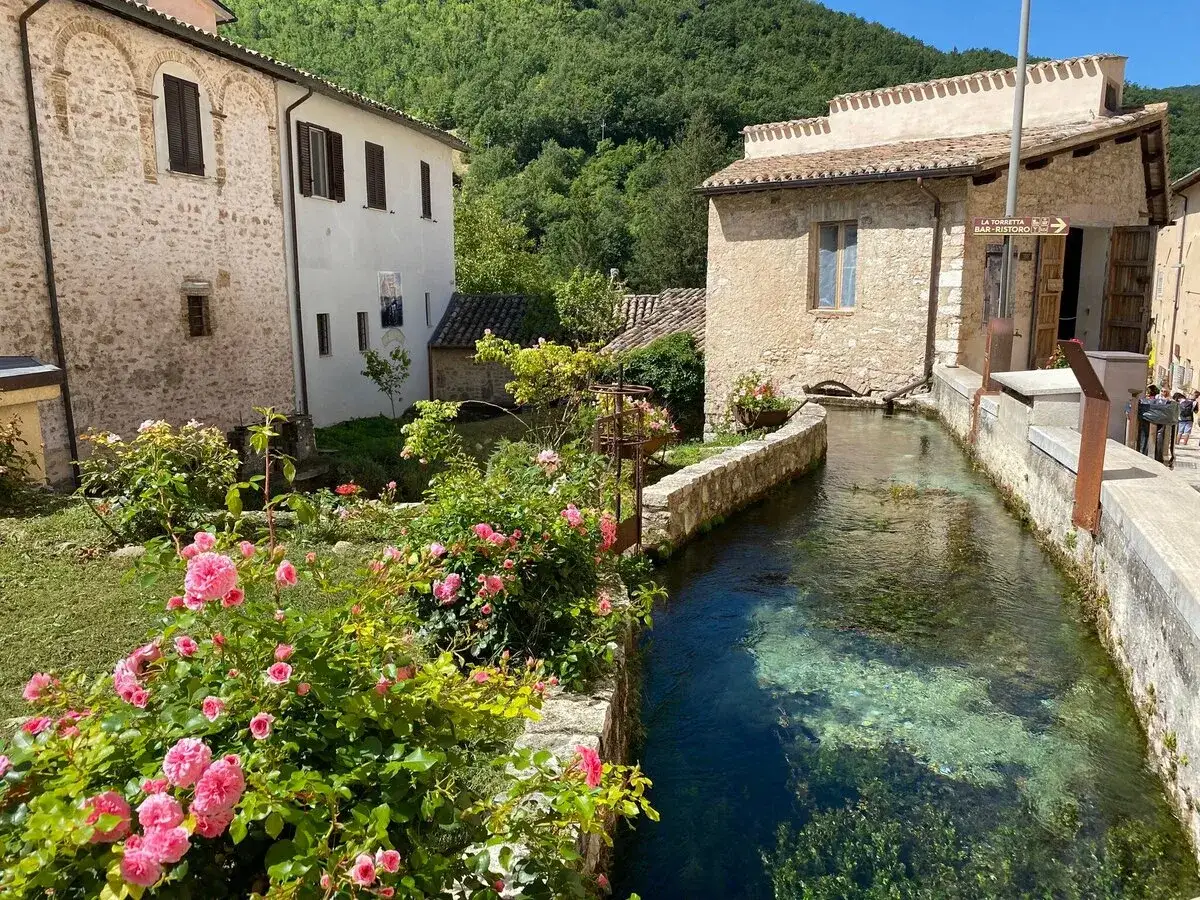 Un incantevole borgo italiano, ideale per 2 giorni nei borghi più belli d'Italia. Un ruscello cristallino attraversa il paese, fiancheggiato da case in pietra e rose rosa.