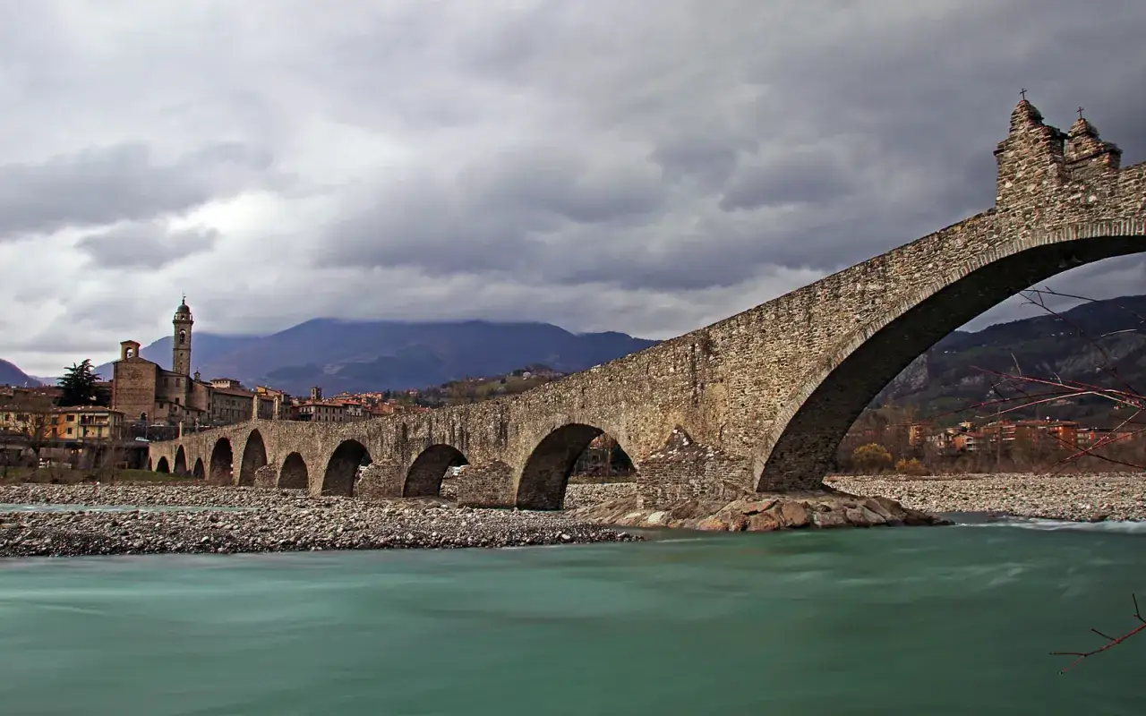 Ponte Gobbo, simbolo di Bobbio borgo dei borghi, attraversa il fiume con le sue arcate storiche sotto un cielo nuvoloso.