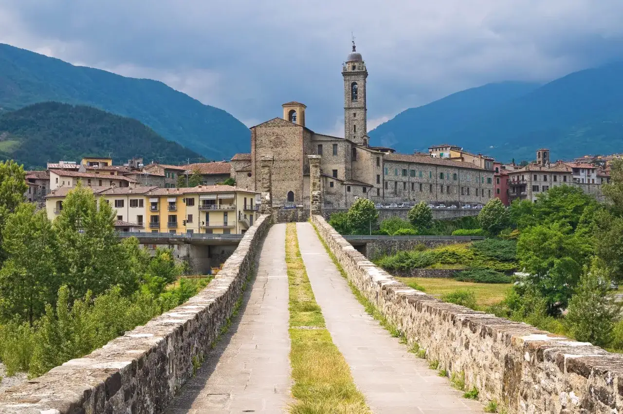 Ponte medievale che conduce a un borgo con chiesa e campanile, ideale per escursioni in Emilia Romagna.