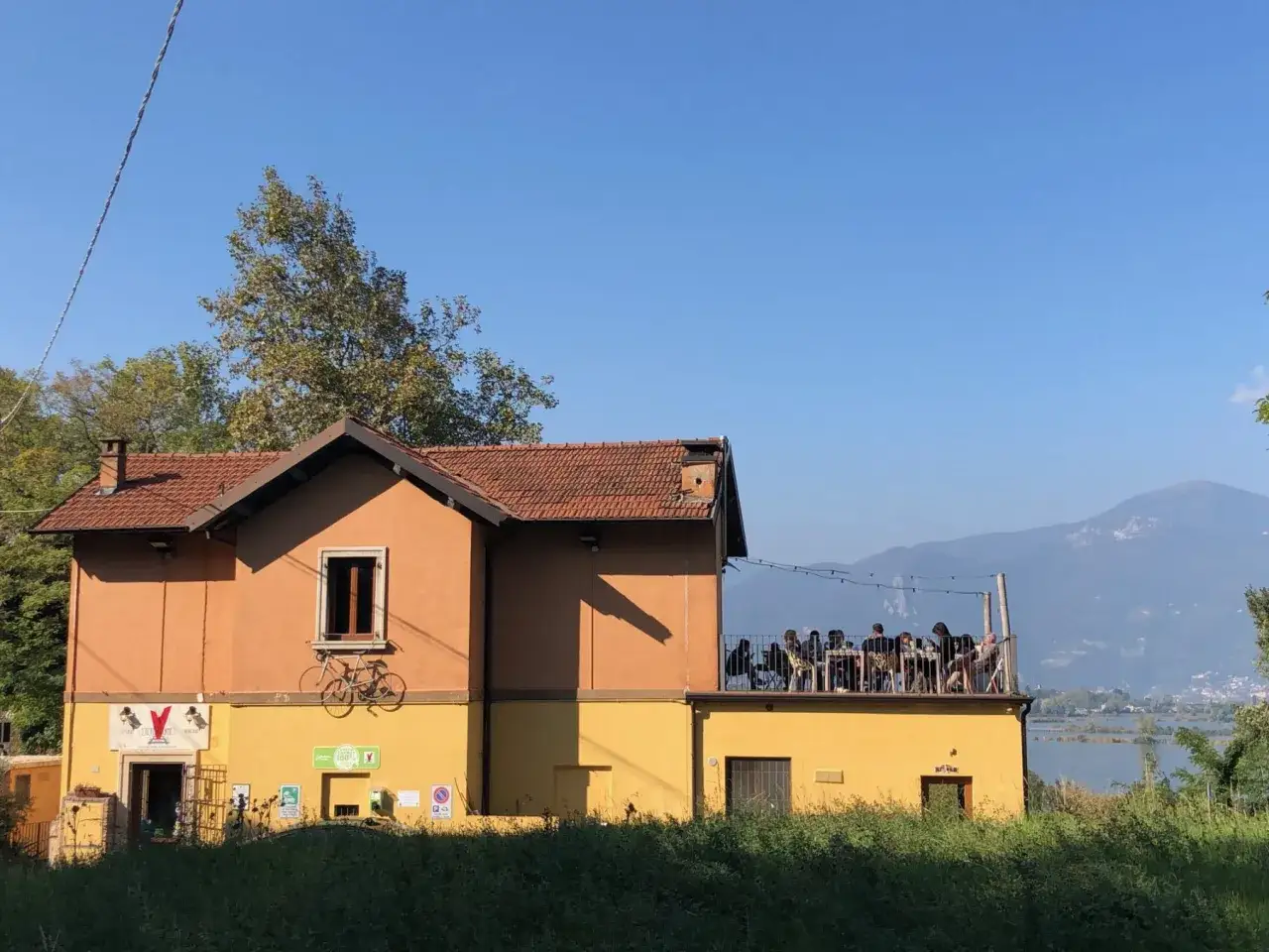 Un locale con terrazza panoramica, dove si trova la Franciacorta, con persone sedute ai tavoli e vista su lago e montagne.