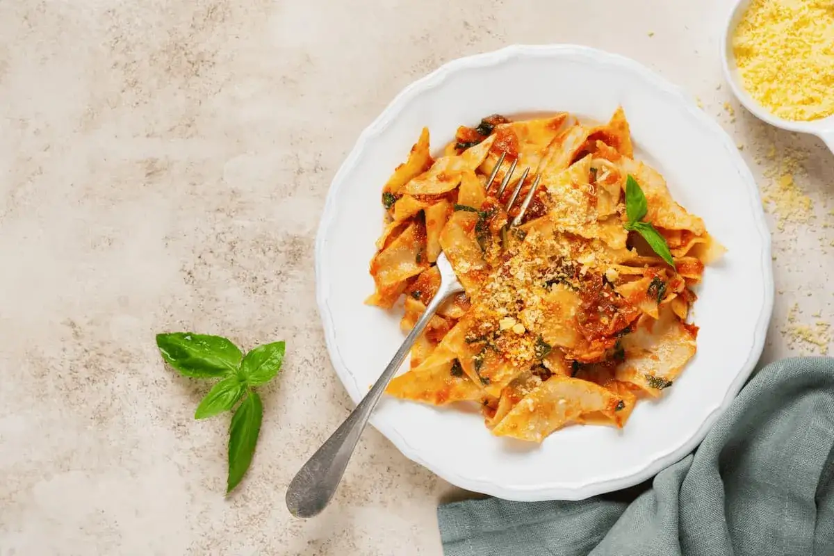Piatto di pasta fresca al ragù, un'ottima idea su cosa mangiare a Ravenna. Guarnita con basilico e parmigiano.