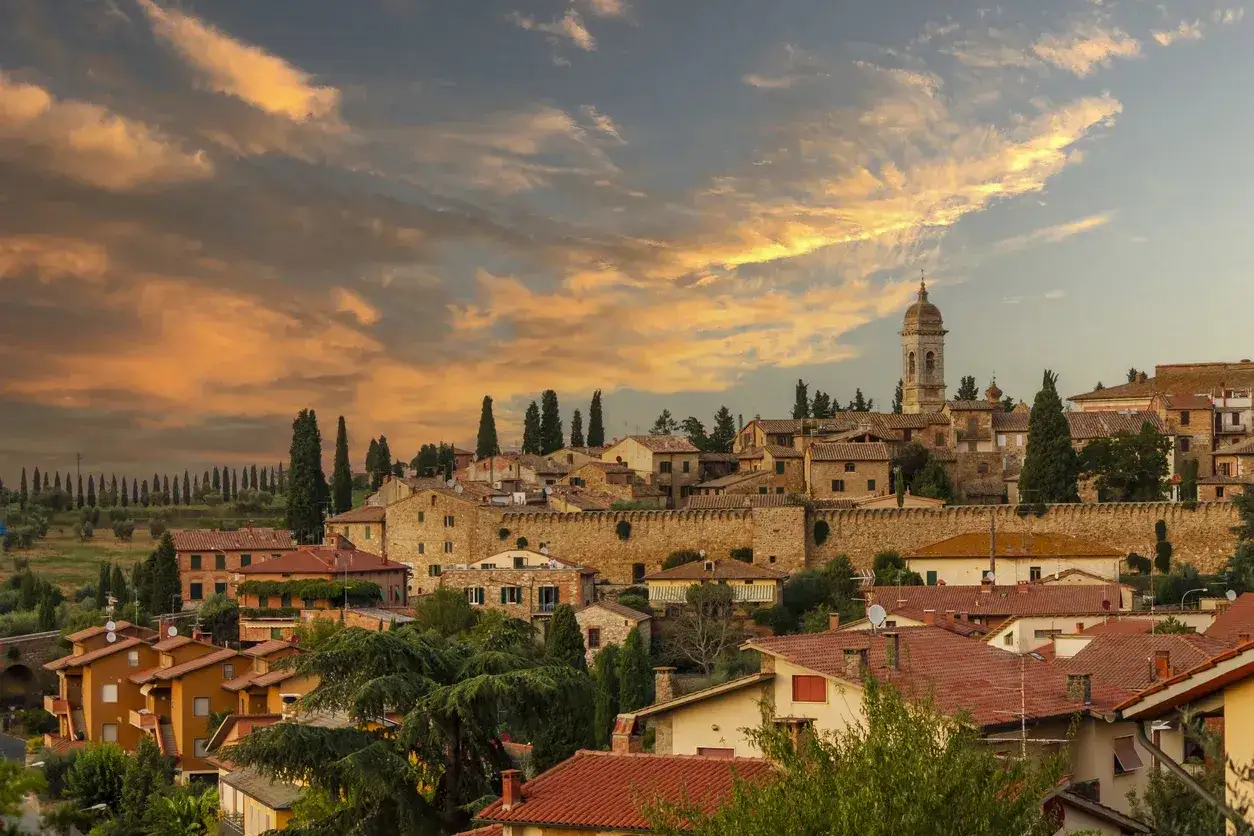 Panoramica di San Quirico d'Orcia al tramonto, con il borgo medievale e la torre campanaria. Un luogo incantevole da scoprire, tra colline toscane e cipressi.