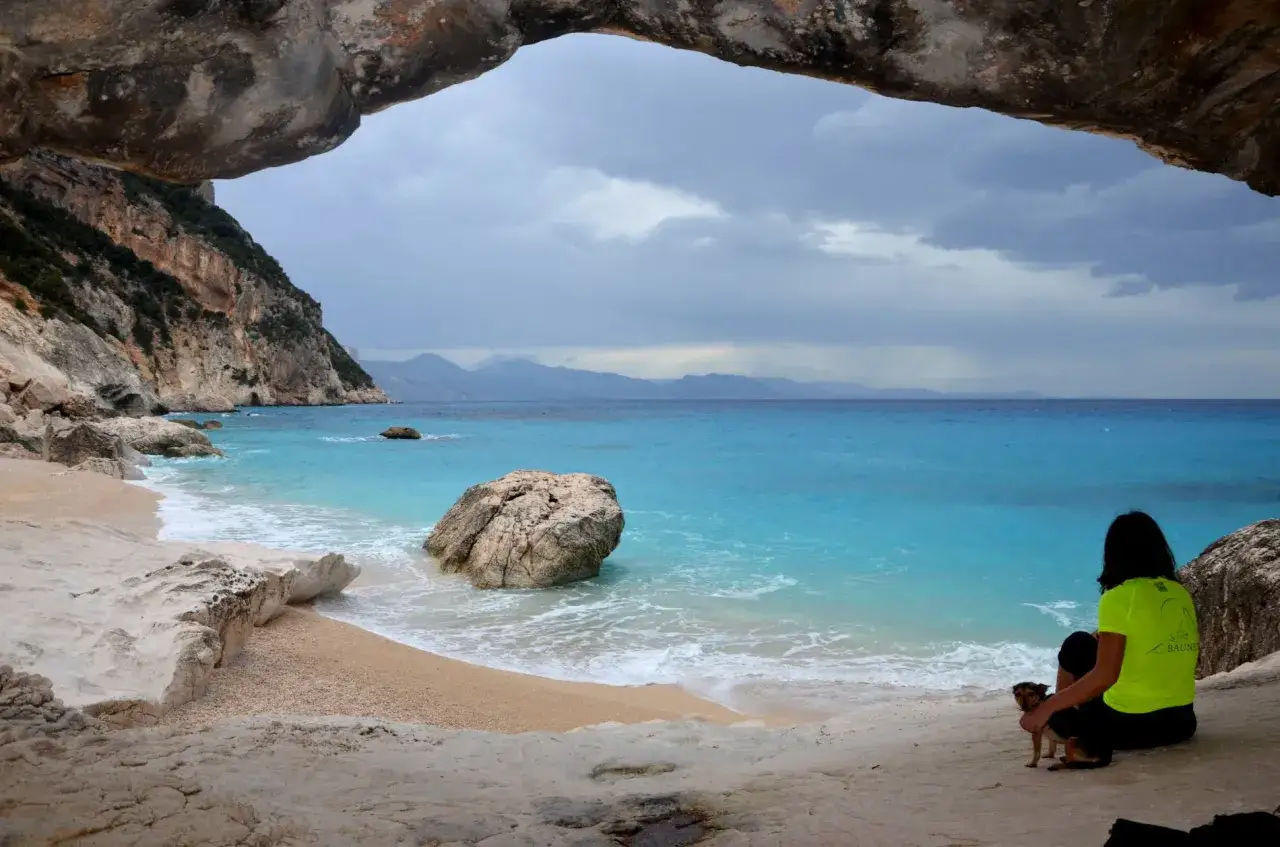 Vista dalla grotta di Cala Goloritzè, raggiungibile con un percorso a piedi. Una donna con un cane ammira il mare turchese.