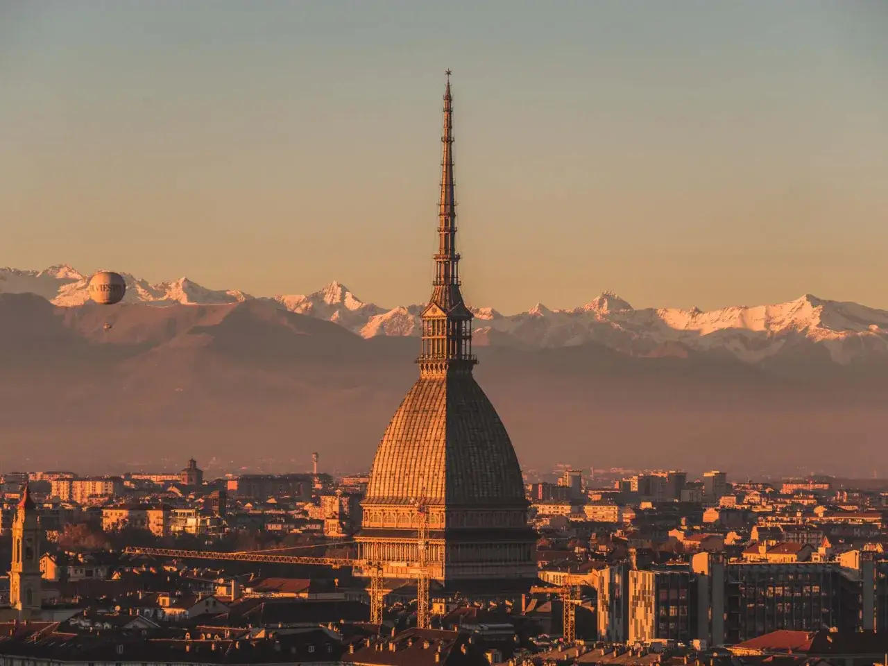 La Mole Antonelliana domina Torino al tramonto, con le Alpi innevate sullo sfondo. Un pallone aerostatico galleggia nel cielo: ecco cosa vedere a Torino in un giorno!