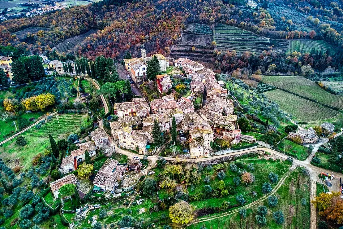 Un borgo medievale tra i vigneti e gli ulivi, un'immagine che evoca le vie del Chianti, con i suoi tetti in cotto e la natura che abbraccia le case.