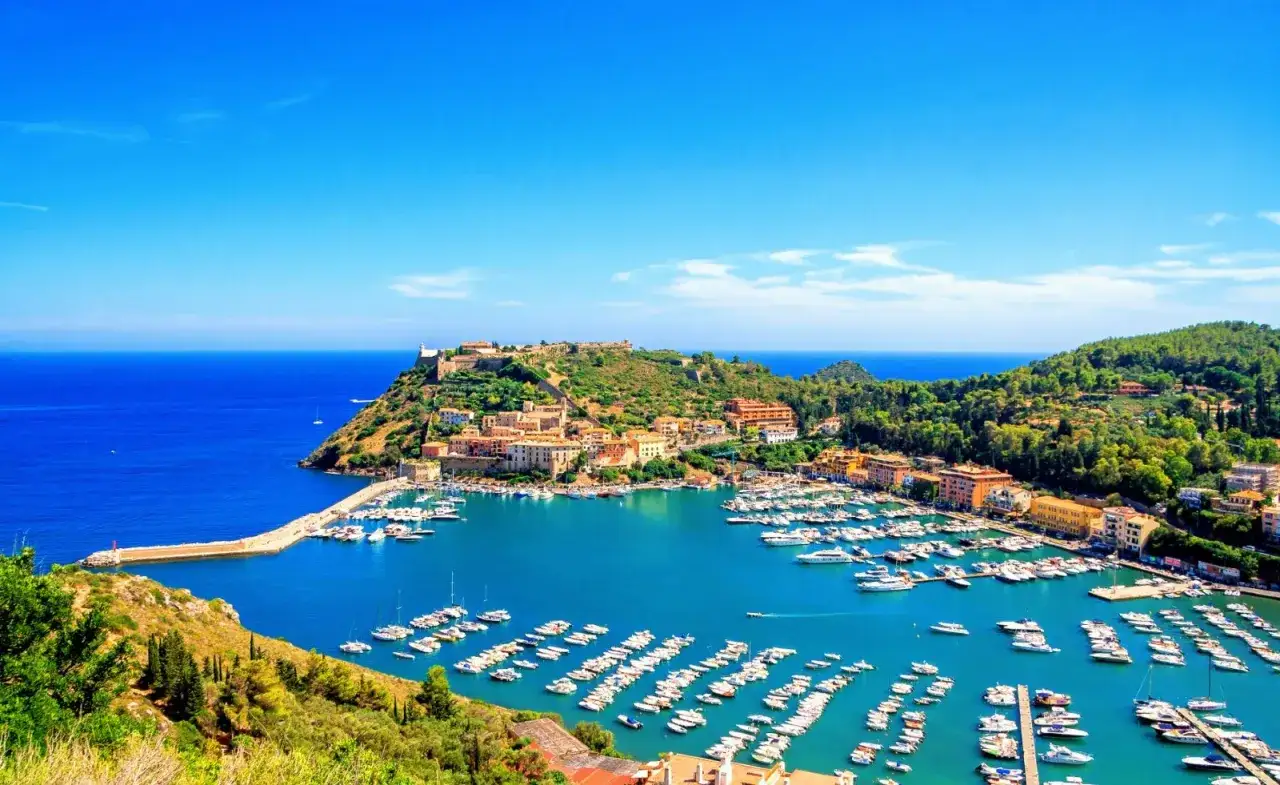 Porto Ercole: un incantevole borgo con un porto pieno di barche, circondato da colline verdi e affacciato sul mare blu. Le spiagge vicine invitano al relax.