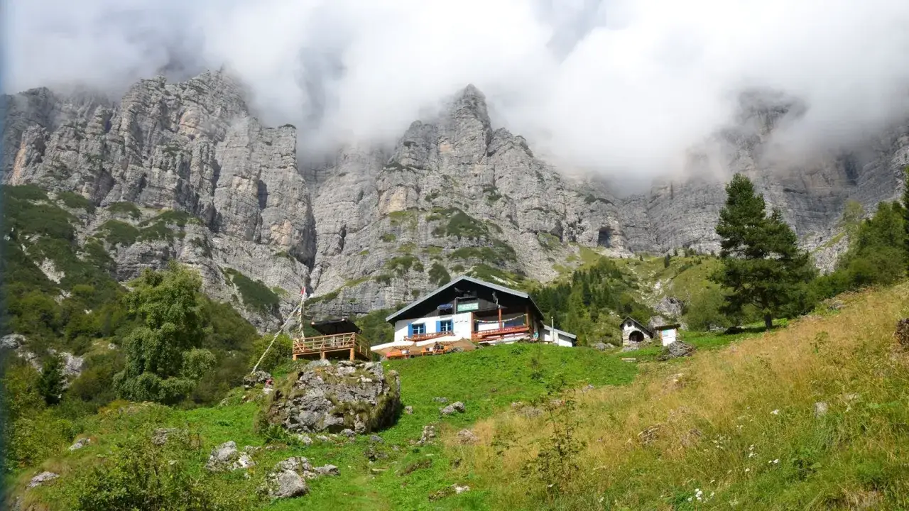 Rifugi in Veneto incastonati tra maestose pareti rocciose, con nuvole che accarezzano le cime. Un'oasi di pace alpina.