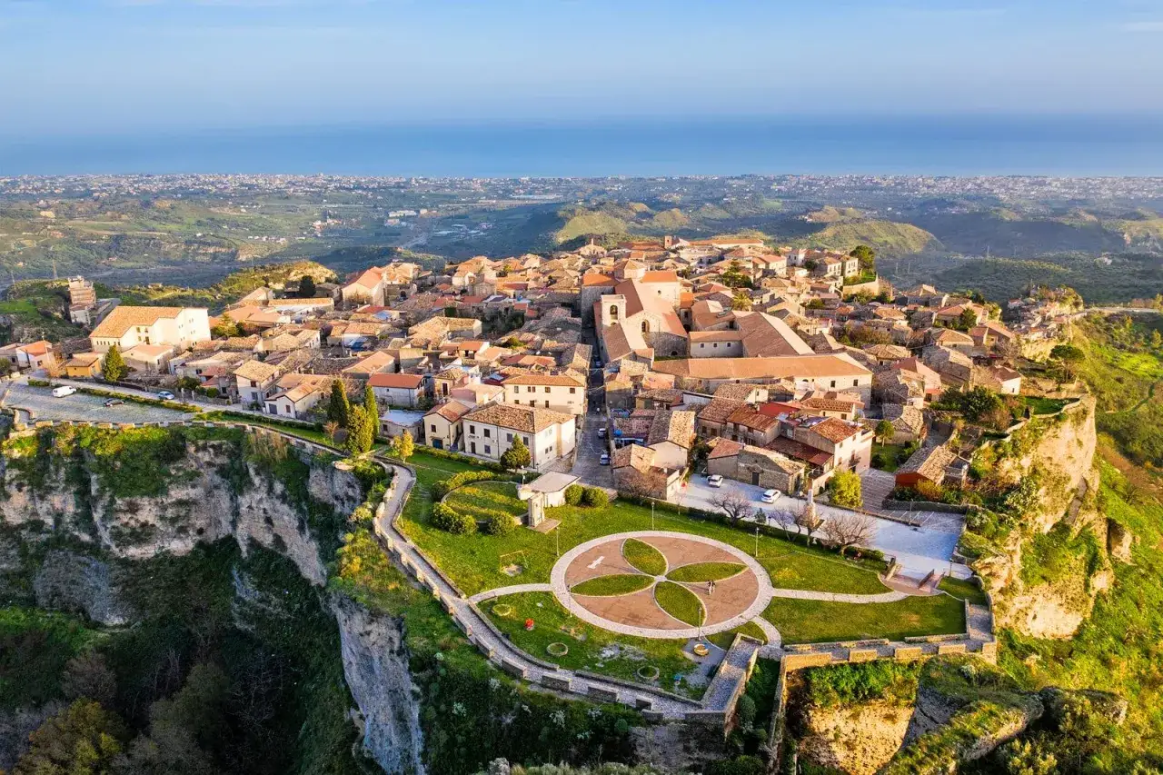 Panoramica aerea di un pittoresco borgo arroccato su una scogliera, uno dei tanti borghi da visitare in Calabria, con case in pietra e tetti rossi che si affacciano sul mare.