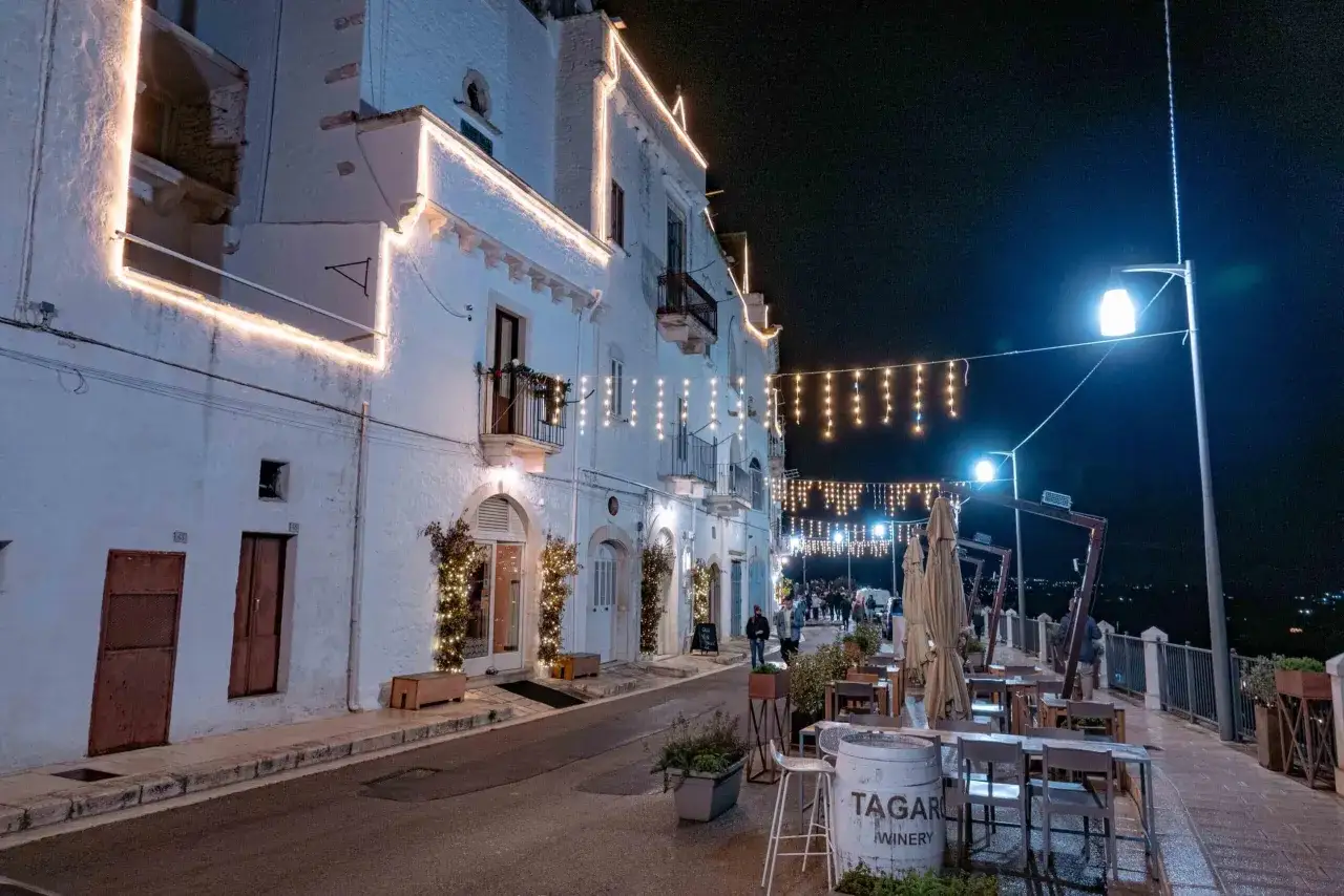 Un incantevole locorotondo di sera, con luci natalizie che illuminano i bianchi vicoli e creano un'atmosfera magica. Tavolini all'aperto invitano a godersi la quiete notturna.
