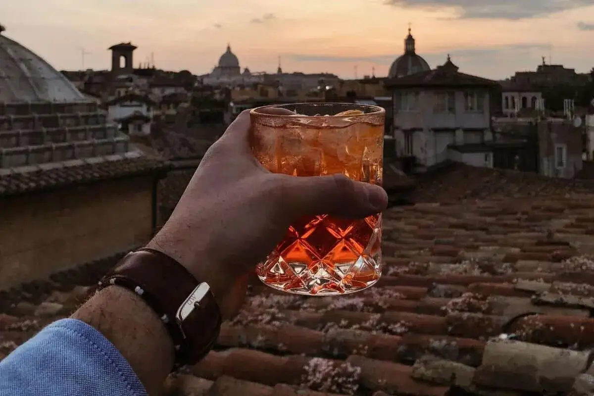 Un bicchiere di Aperol Spritz con vista sui tetti di Roma centro al tramonto. Un momento perfetto per un apericena.