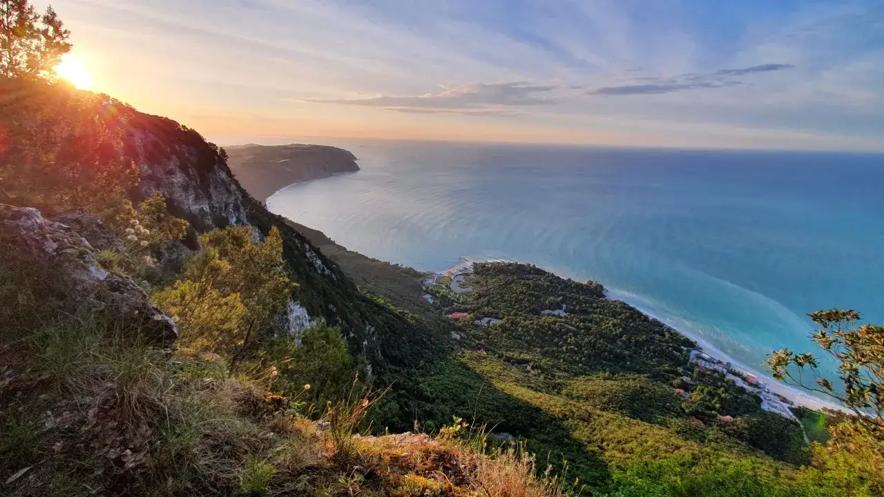 Alba sui sentieri del Monte Conero, con il sole che illumina la costa e il mare Adriatico.