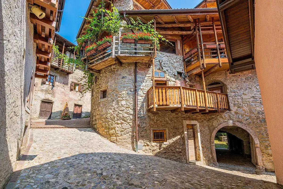 Un vicolo acciottolato tra antiche case in pietra con balconi in legno fioriti, tipici dei borghi Trentino Alto Adige.