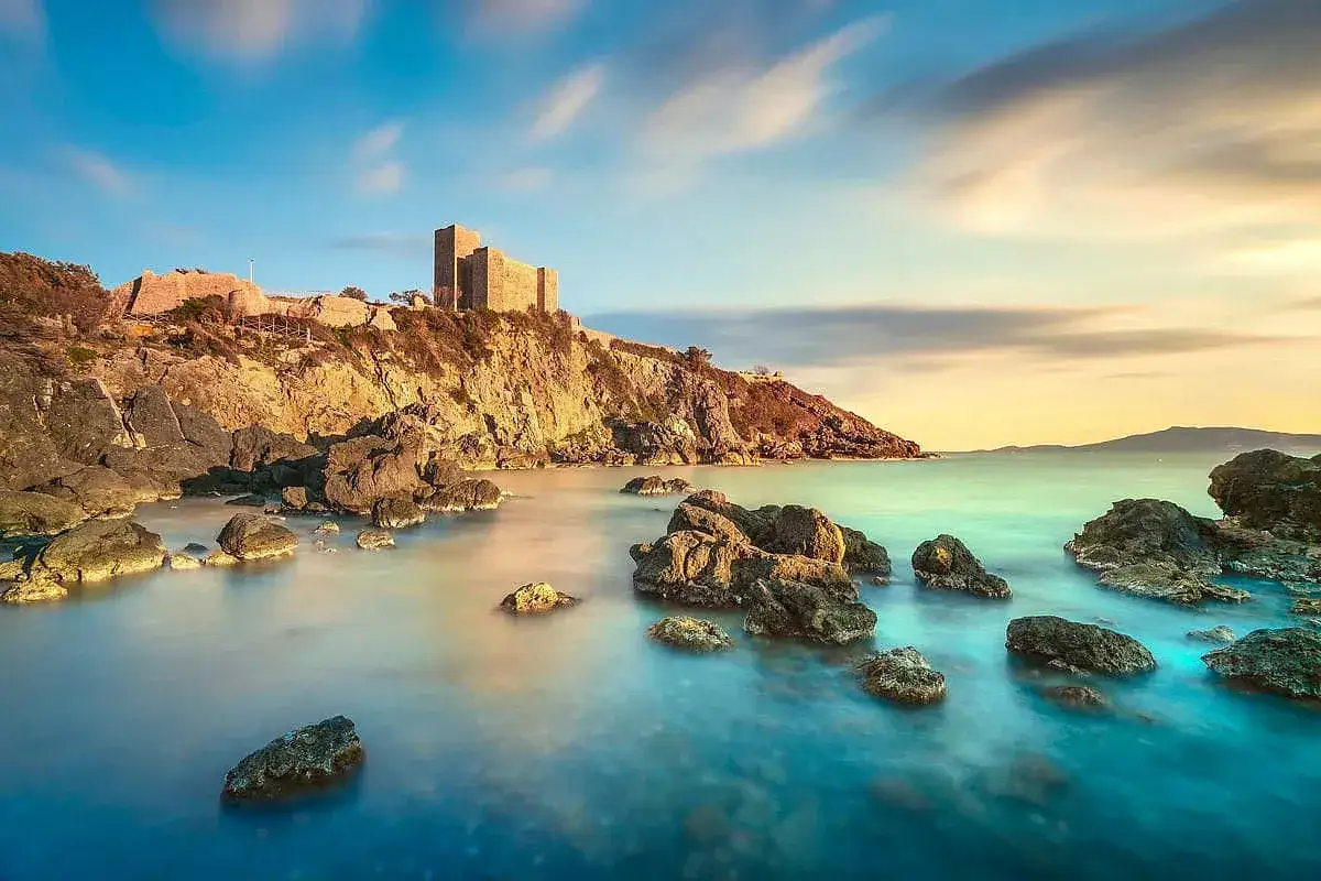 Rocche e castello sulla costa, un'immagine iconica di cosa vedere in Maremma. Acque calme e cielo suggestivo.