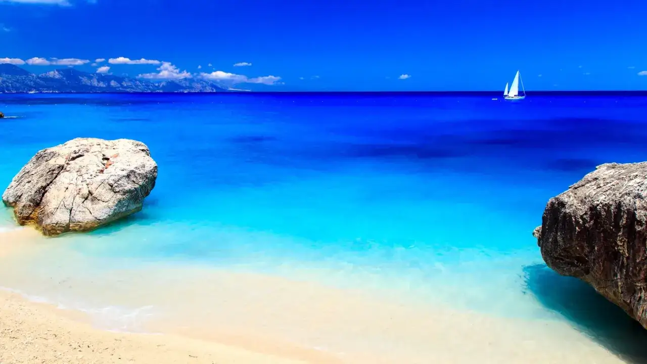 Spiaggia bianca, mare cristallino e rocce imponenti: un angolo di paradiso tra le spiagge più belle d'Italia. Una vela bianca all'orizzonte.