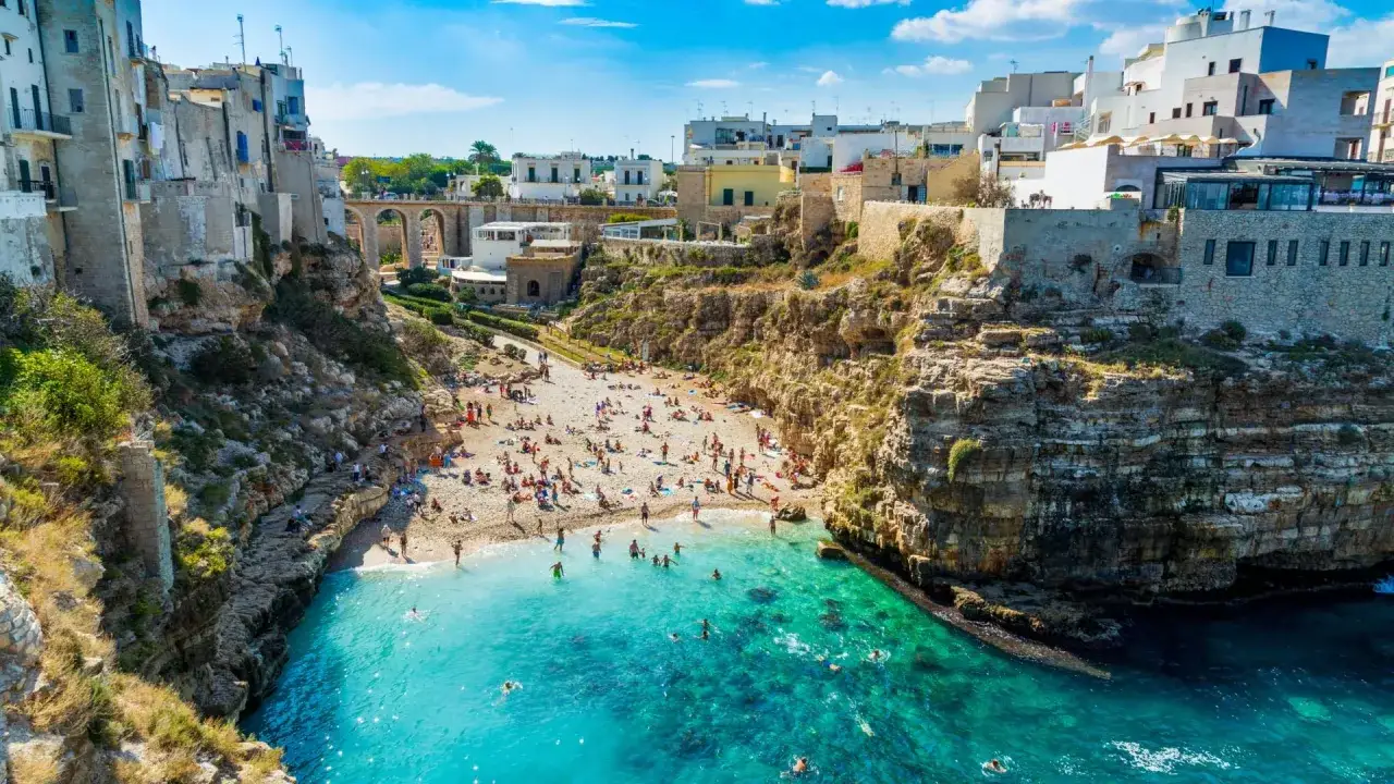Una baia con spiaggia affollata e case bianche a picco sul mare turchese, un gioiello tra le spiagge vicino Bari.