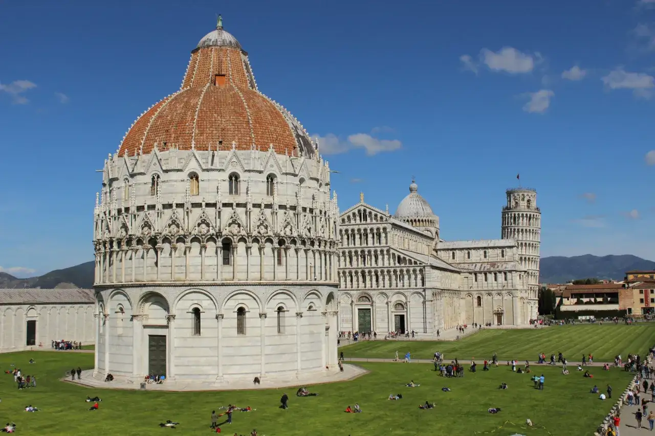 Il Battistero e il Duomo di Pisa, con la celebre Torre Pendente che mostra perchè la torre di Pisa è storta, su un prato verde affollato.