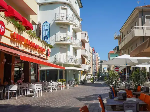 Passeggiata serale a Gabicce Mare: tavolini all'aperto di un caffè, hotel Lido e negozi colorati.