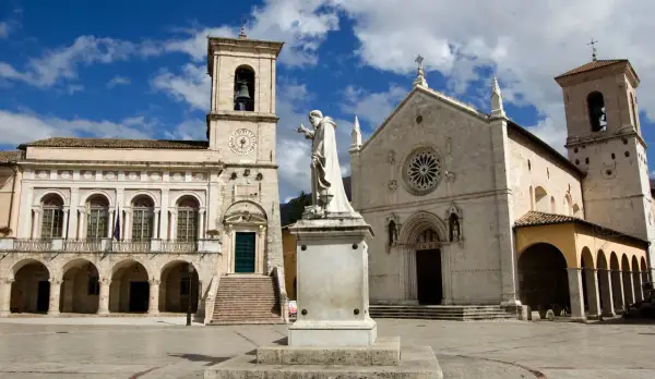 La piazza di Norcia con la basilica e il palazzo comunale, dominata dalla statua di San Benedetto. La basilica di Norcia oggi si presenta maestosa.