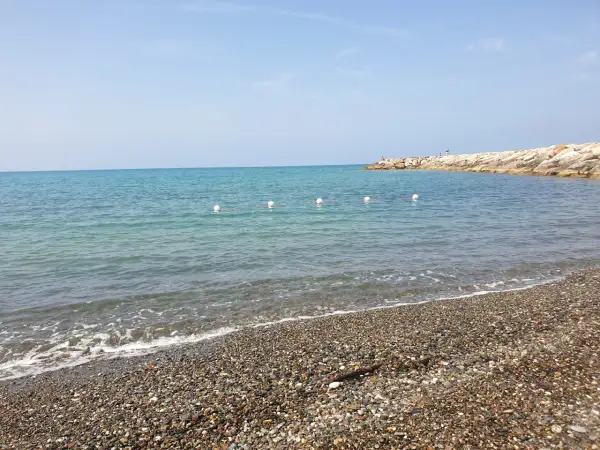 Spiaggia di ciottoli a Cecina, con mare calmo e un molo in lontananza. Perfetto per scoprire cosa vedere e rilassarsi.