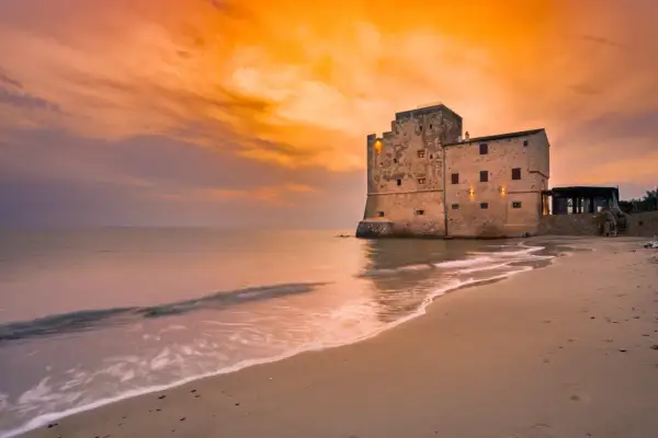 Spiaggia Torre Mozza Follonica: tramonto dorato su antica fortezza sul mare. Come arrivare: facile accesso dalla strada costiera.