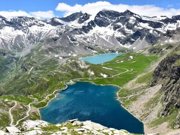 Laghi alpini e strada tortuosa sul colle del Nivolet, con montagne innevate sullo sfondo.