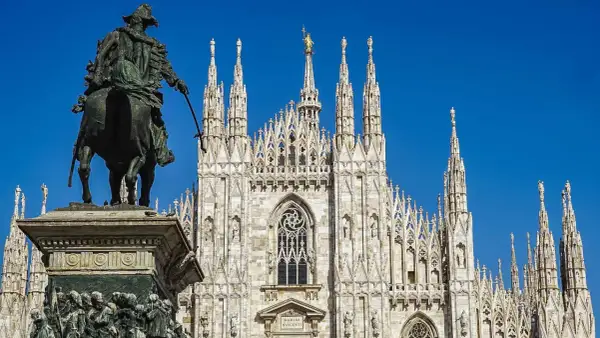 Statua equestre davanti al maestoso Duomo di Milano, con le sue guglie che svettano verso il cielo azzurro.