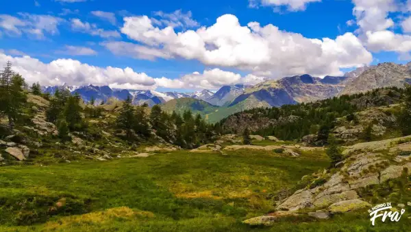 Val Seriana: un prato verde e rocce ai piedi di montagne innevate, ideale per passeggiate facili e rigeneranti.