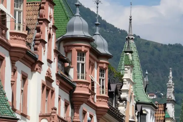 Edifici storici con torrette e tetti verdi, un assaggio di cosa vedere a Bolzano in un giorno, con montagne sullo sfondo.