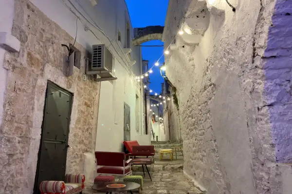 Un vicolo suggestivo con luci soffuse, sedute colorate e un arco in pietra. Perfetto per scoprire cosa vedere vicino Alberobello.