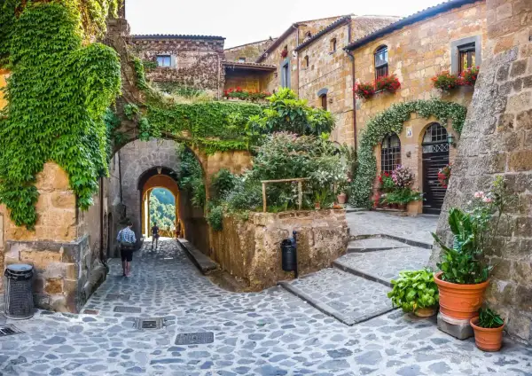Un vicolo acciottolato tra antichi edifici ricoperti di edera e fiori, un invito a scoprire i borghi da visitare nelle Marche.