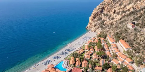 Villaggio turistico con spiaggia attrezzata e piscina, incastonato tra il mare blu e una scogliera rocciosa. Un luogo ideale per esplorare i paesi vicino Catania sul mare.