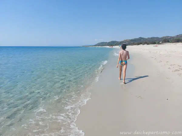 Bambino cammina sulla spiaggia della costa est Sardegna, mare cristallino e cielo azzurro.
