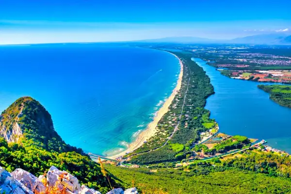 Vista mozzafiato di una spiaggia dorata e un fiume blu intenso, con montagne verdi sullo sfondo. A Roma c'è il mare, un paradiso terrestre.