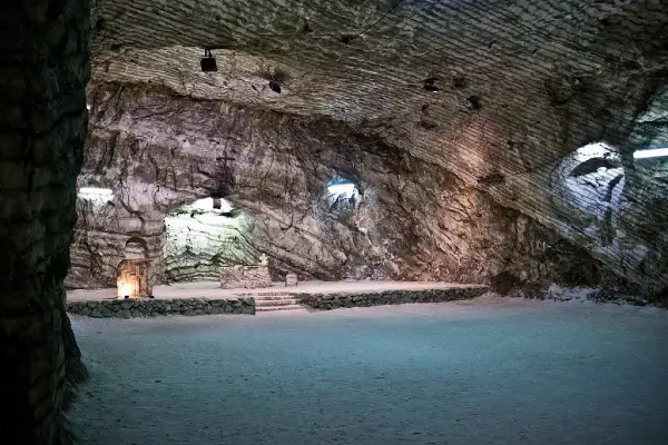 Interno della cattedrale di sale di Realmonte, con pareti rocciose stratificate e un altare illuminato.