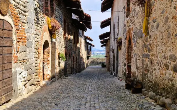 Antico vicolo lastricato nel ricetto di Candelo, con case in pietra e mattoni, archi e porte in legno.