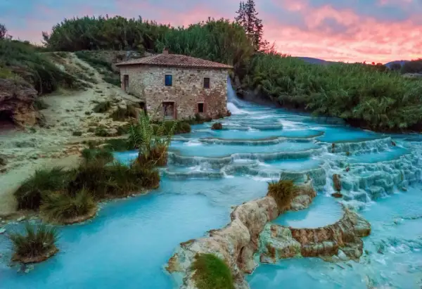 Cascate termali turchesi con un antico mulino in pietra, uno dei tanti posti belli in Toscana, al tramonto.