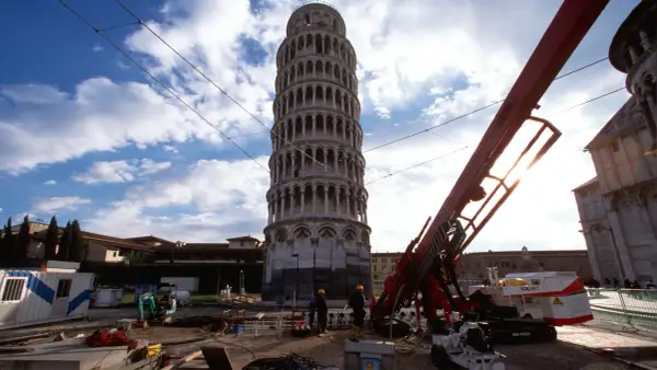 La Torre di Pisa prima e dopo i lavori di consolidamento: un cantiere con macchinari e operai accanto alla torre pendente.