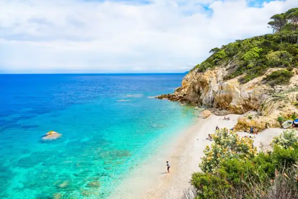 Spiaggia incantevole con acque cristalline, rocce dorate e vegetazione lussureggiante. Un angolo di paradiso, quasi un mare vicino Firenze, dove rilassarsi.